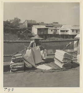Man selling cloth by the river at Tai'an with houses on stilts in the background
