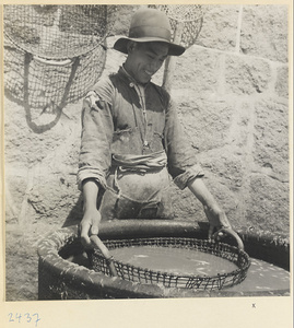 Man holding a sieve in a barrel in a fishing village on the Shandong coast