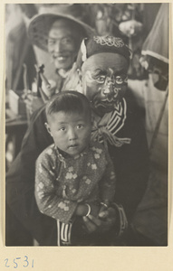 Actor holding a child at a market fair during the Dragon Boat Festival in a village on the Shandong coast