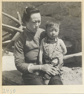 Women holding a child wearing a braided necklace and an embroidered purse in a fishing village on the Shandong coast