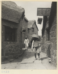 Men walking in a street next to stone buildings and shop sign for a barber shop (top) in a village on the Shandong coast