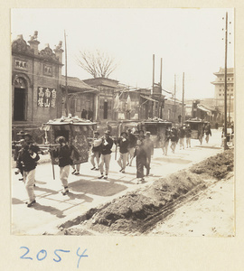 Members of a wedding procession carrying three sedan chairs past shops near city gate, Beijing