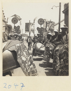 Members of a wedding procession playing drums and carrying draped mirrors, fan-shaped screens, and umbrellas