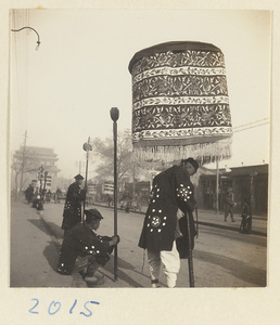 Members of a funeral procession holding embroidered umbrellas and staffs