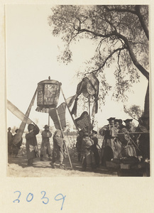 Members of a wedding procession standing with umbrella, fan-shaped screens, draped mirror, and musical instruments