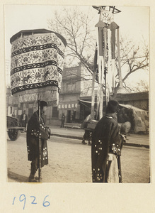 Members of a funeral procession with umbrella and inscribed banner