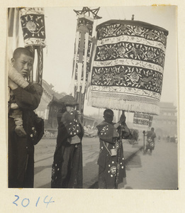 Members of a funeral procession carrying embroiderd umbrellas and banners in funeral procession