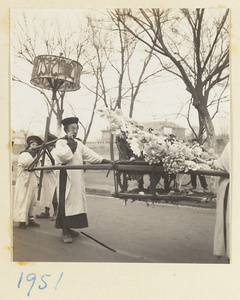 Members of a funeral procession carrying umbrella and empty sedan chair decorated with a paper wreath