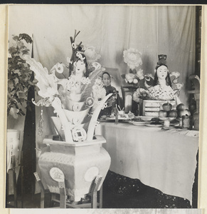 Funeral altar with paper figures, coins, photograph of the deceased, and food