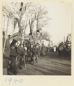 Members of a funeral procession carrying flags, umbrellas, and musical instruments