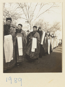 Buddhist monks and nuns carrying musical instruments and cloth in a funeral procession