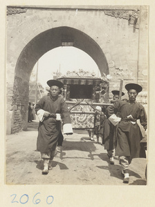 Members of a wedding procession carrying sedan chair through city gate