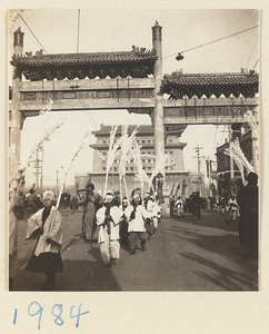 Members of a funeral procession carrying paper snow willows under pai lou near city gate