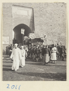 Mourners dressed in white proceeding draped coffin through city gate during funeral procession