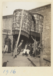 Members of a funeral procession with umbrellas resting by a wall