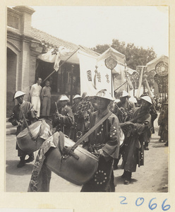 Members of a wedding procession playing musical instruments and carrying draped mirrors, fan-shaped screens, and umbrella past inscribed banner