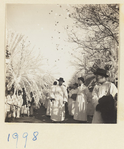 Members of a funeral procession carrying paper snow willows and tossing paper money in the air