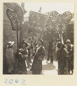 Members of a wedding procession carrying fan-shaped screens and umbrellas