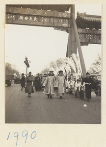 Members of a funeral procession passing under pai lou carrying snow willows and banners