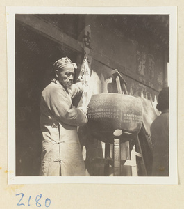 Man holding an inscribed banner and standing next to an inscribed metal bell on Miaofeng Mountain