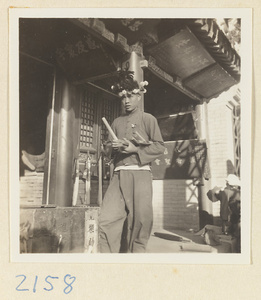 Boy wearing a souvenir hat and holding bundles of incense outside temple with inscriptions on the pilgrimage trail on Miaofeng Mountain