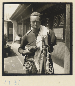 Man holding incense and rope outside temple building on Miaofeng Mountain