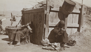 A man resting on a chair and a woman mending clothes near the waterfront, Hong Kong