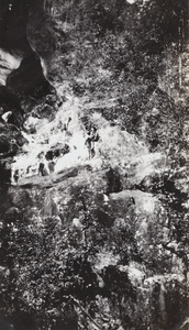 Three men wearing bathing costumes on a rocky ledge of a waterfall