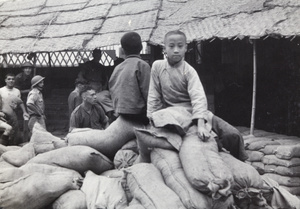 Two boys sitting on sandbags as British soldiers build defences, Shanghai, 1937