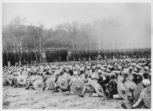 Seated Eighth Route Army soldiers, with bamboo hats, listening to a speaker on a stage