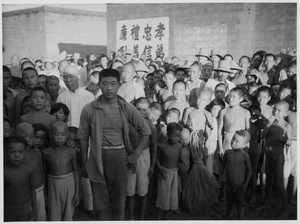 Group of children and others in front of principles of conduct painted on a wall (The Four Cardinal Principles)