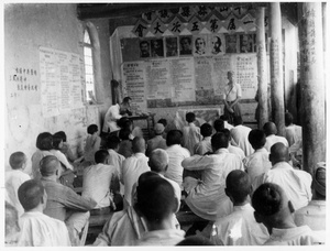 An unidentified foreigner addressing men in a room decorated with portraits of Stalin, Marx, and others