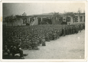 Mass outdoor meeting with stage and large Chinese characters on the walls