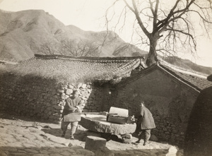 Two women with bound feet turning a millstone, near Beijing