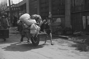 Woman reading on a wheelbarrow loaded with domestic possessions