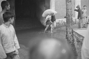 Porter carrying sack through floodwaters, Shanghai