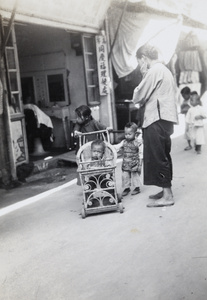 Children with a wicker pram, outside a barber, Xiamen