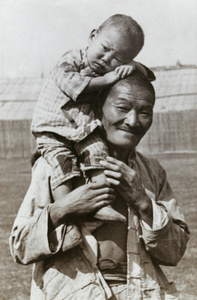 A smiling Chinese man with a boy perched on his shoulder