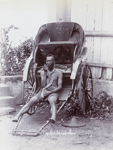 A Chinese rickshaw puller having a smoke, with a rickshaw, Singapore