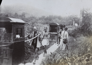 Sedan chairs and bearers on a path near pailou